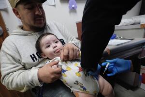 César Acevedo sostiene a su hijo Adriel mientras una enfermera le administra una vacuna en la clínica de inmunización de Salud y Servicios Humanos del Condado de Dallas en Dallas, el viernes 4 de abril de 2025. 