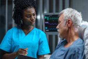 In the Hospital, Senior Patient Lying in the Bed Talking to a Nurse who is Holding Tablet Computer Showing Him Information. In the Technologically Advanced Hospital Ward.