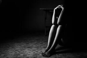 a woman sitting on ground with arm around lower head, sexual violence , sexual abuse, human trafficking concept