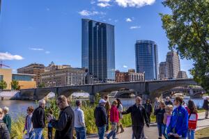 People stroll along the Grand River with Grand Rapids skyline