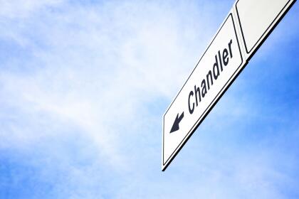 White signboard with an arrow pointing left towards Chandler, Arizona, USA, against a hazy blue sky in a concept of travel, navigation and direction. Path included for the signboard