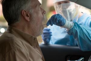 A medical technician in full protective gear collects a sample from a mature man sitting inside his car as part of the operations of a coronavirus mobile testing unit..
