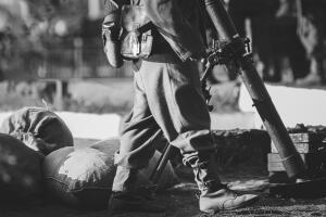 Close-up View On Re-enactor Dressed As German Wehrmacht Infantry Soldier In World War Ii With Submachine Gun Mp 40 Patrols Territory Of Mortar Crew. German Soldier Guards Mortar. Black And White