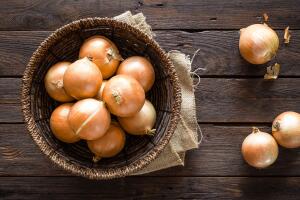 Fresh onion in basket on wooden table, top view