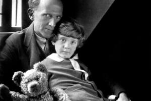 A portrait of the author AA Milne sat with Christopher Robin and the bear Winnie the Pooh Grosby.jpg