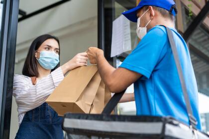 Asian Food deliverly man wear protective mask due to Covid-19 pandemic, receive beverage order from restaurant worker at coffee shop. Waitress give takeaway bag to postman for new normal lifestyles.