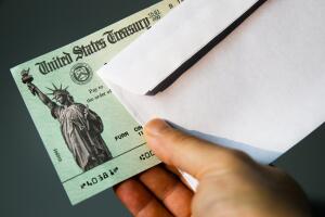 United States Treasury check surrounded by US currency.  Illustration for stimulus package checks expected to ease the impact of Corona Virus (Covid-19) restrictions or IRS income tax refund.