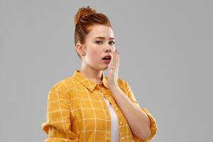 red haired teenage girl covering mouth by hands