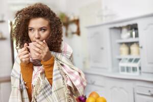 Young woman wrapped in blanket drinking hot tea