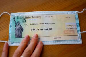 Stimulus relief program check over medical mask in hand.  Close up view