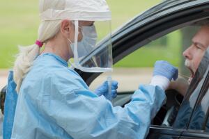 Dressed in full protective gear a healthcare worker collects a sample from a mature man sitting inside his car as part of the operations of a coronavirus mobile testing unit...