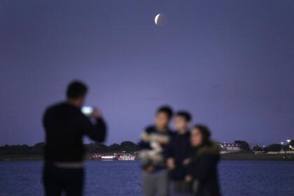 Members of Prieto Yegros family take pictures as they watch the moon in partial eclipse in Asuncion's Bay, Paraguay, early Friday, Nov. 19, 2021. (AP Photo/Jorge Saenz)