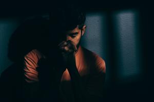 Prisoner man in dark cell depressed or praying