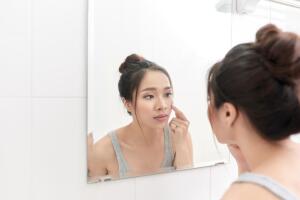 Skin care. Woman applying skin cream on her face in front of mirror