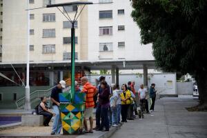 People line up as others charge their phones with a solar panel at a public square in Caracas