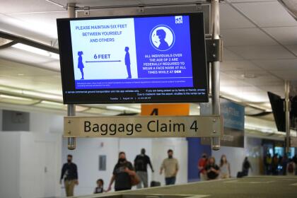 A message about COVID-19 restrictions illuminates the screen of a monitor over a baggae carousel as travelers move through the main terminal of Denver International Airport Tuesday, Aug. 24, 2021, in Denver. (AP Photo/David Zalubowski)