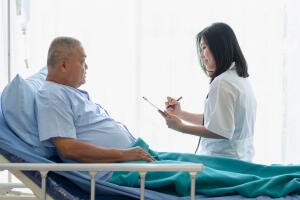 Senior Asian man receiving medical check up or health condition interview from a doctor in a hospital room.