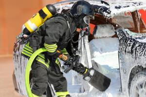 Firefighter with oxygen tank while spraying white extinguishing foam to put out the fire that broke out in the car after the road accident