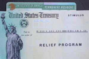 Permanent resident card of United States of America next to the Stimulus Check relief program. Benefits for green card holders concept.