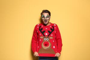 Young man in Christmas sweater with party glasses on color background 