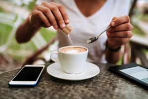 Young woman adding white sugar to the coffee.