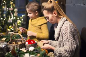 Woman with girl decorating coniferous wreath