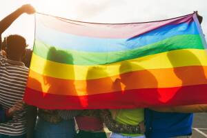 Young diverse people having fun holding lgbt rainbow flag outdoor - Main focus on african guy back