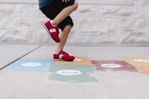 Low section side view of boy in red trainers playing hopscotch.