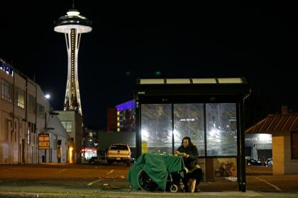 In this Oct. 30, 2017 photo, Dave Chung, who says he has been homeless for five years on the streets of California and Washington state, eats a meal before bedding down in a bus shelter in view of the Space Needle in Seattle. Chung says he has been offered shelter many times, but chooses to remain outside due to the living conditions in homeless shelters and conflicts he has with other people. (AP Photo/Ted S. Warren)