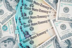 Us dollar bills scattered around on table with  us treasury checks in top. To illustrate the financial help from th us government during the covid-19 crisis.