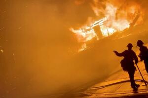 A firefighter gestures to a colleague in front of a house on fire during wildfires in San Bernardino, California