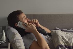 Sick man in bed next to his medications in his home talking on the phone. Man suffering cold and winter flu virus