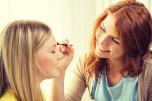 two smiling teenage girls applying make up at home