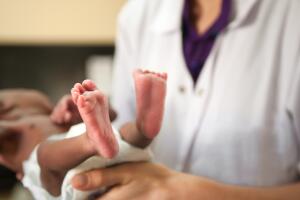 Doctor is holding tiny baby, feet are visible.
