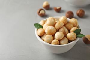 Bowl with shelled organic Macadamia nuts and space for text on grey background 