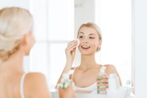 young woman with lotion washing face at bathroom