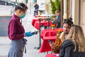 Waitress with a mask and clients at an outdoor bar, café or restaurant