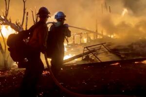 Firefighters direct water on a burning house during wildfires in San Bernardino, California