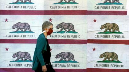 Una mujer camina frente a carteles con la bandera de California en una calle de la ciudad de San Francisco.