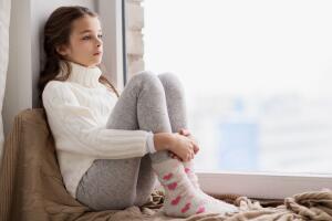 sad girl sitting on sill at home window in winter