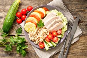 Healthy vegetable buddha bowl lunch with turkey, vegetables and quinoa on brown wooden background. Top view.