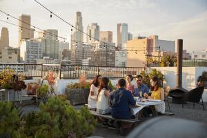 Friends Gathered On Rooftop Terrace For Meal With City Skyline In Background