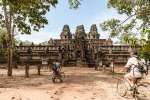 Tourist couple cycling around Angkor temple, Cambodia. Ta Keo building ruins in the jungle. Eco friendly tourism traveling, toned image.