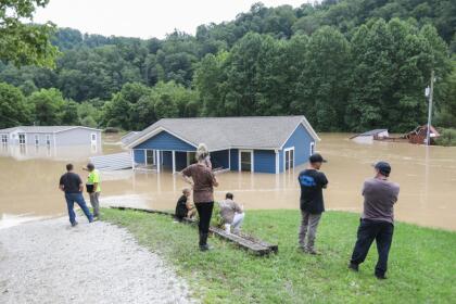 Family look at their home submerged under flood waters from the North Fork of the Kentucky River in Jackson, Kentucky, on July 28, 2022. - At least three people have died after torrential rains caused massive flooding in eastern Kentucky, leaving a number of people stranded on rooftops and in trees, the governor of the southeastern US state said Thursday. (Photo by LEANDRO LOZADA / AFP) (Photo by LEANDRO LOZADA/AFP via Getty Images)