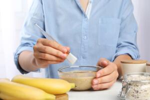 Woman with handmade face mask, brush and ingredients at white wooden table, closeup 
