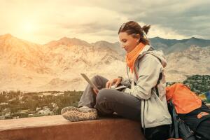 Backpacker with laptop sits on the top view point under mountain