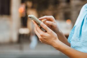 Close-up photo of female hands with smartphone. Young woman typing on a mobile phone on a street