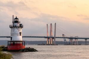 Panorama of a caisson (sparkplug) style lighthouse under soft golden light with a bridge in the background.