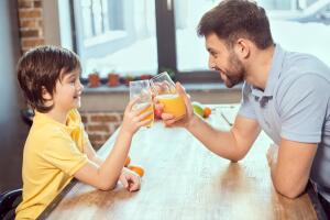 Side view of happy father and son drinking fresh juice together
