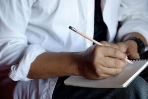 Cropped shot of man writing on paper notebook with pencil
